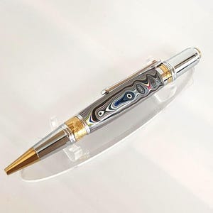 May include: A silver and gold pen with a unique patterned design. The pen features a gold-colored tip and accents, with a silver clip and top. The body of the pen has a swirling pattern of silver, black, and blue.