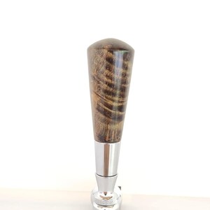 May include: A beer tap handle with a wooden top and a chrome base. The wooden handle has a dark brown and gold grain pattern. The chrome base has a lever and a circular knob.