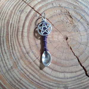 Puede incluir: Una cuchara de plata con un alambre morado envuelto alrededor del mango. La parte superior del mango tiene un círculo plateado con una estrella de cinco puntas en su interior.