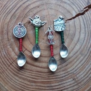 Puede incluir: Cuatro cucharas de plata con diferentes amuletos de personajes de Star Wars. Los amuletos son Yoda, un caza TIE, un casco de Stormtrooper y la Estrella de la Muerte. Las cucharas están envueltas en hilo rojo y verde.