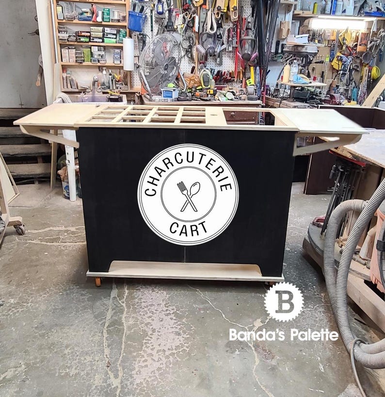 May include: A wooden charcuterie cart with a black chalkboard panel featuring a white logo that says "CHARCUTERIE CART" with a fork and spoon graphic. The cart has a wooden top and shelves.
