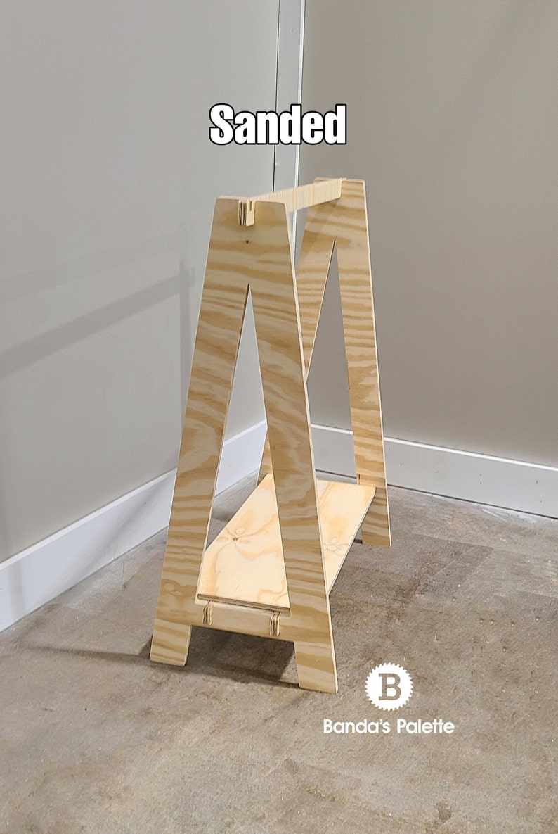 May include: A wooden sawhorse with a natural finish. The sawhorse has an A-frame design with a horizontal shelf. The word "Sanded" is written in white text at the top. The Banda's Palette logo is at the bottom.