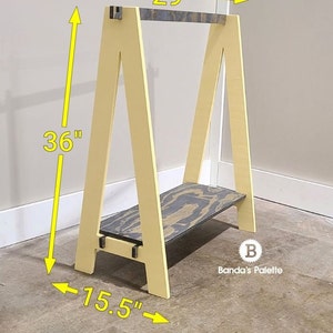 May include: A wooden A-frame shelf in a light yellow color. The shelf is 36 inches tall, 29 inches wide, and 15.5 inches deep. It has a shelf with a black and gray pattern. The shelf is from Banda's Palette.
