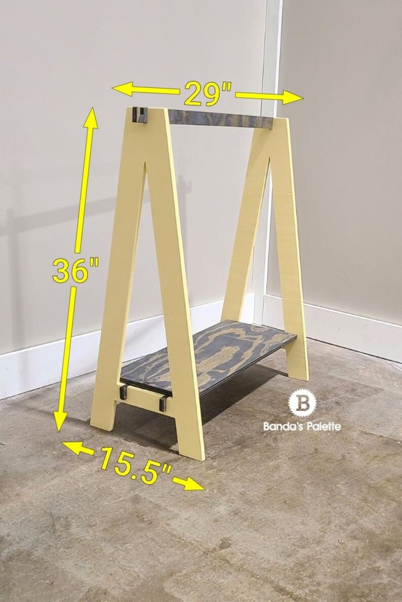 May include: A wooden A-frame shelf in a light yellow color. The shelf is 36 inches tall, 29 inches wide, and 15.5 inches deep. It has a shelf with a black and gray pattern. The shelf is from Banda's Palette.