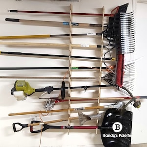 May include: A wooden wall-mounted rack with various gardening tools hanging on it, including rakes, shovels, and a weed trimmer. The rack is made of wood and has a simple design. The tools are all in good condition and ready to use. The rack is labeled "Banda's Palette".
