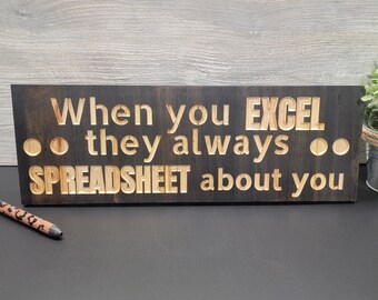 May include: A dark brown wooden sign with the text "When you EXCEL... they always... SPREADSHEET about you".