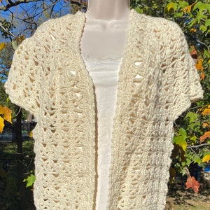 May include: A crocheted cream-colored cardigan with short sleeves and an open front. The cardigan is made with a delicate stitch pattern and has a relaxed fit.