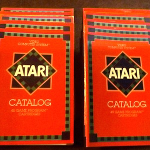 May include: Two stacks of vintage Atari game catalogs. Each catalog features a red cover with the Atari logo in a diamond shape, the words "CATALOG" and "45 GAME PROGRAM CARTRIDGES" or "49 GAME PROGRAM CARTRIDGES".