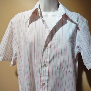 May include: A white short-sleeved button-down shirt with thin pink stripes.