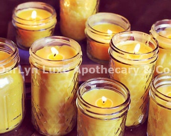 May include: A collection of eight yellow beeswax candles in glass jars. The candles are lit and the wax is melted. The jars have a textured surface.