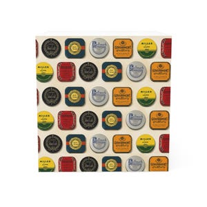 Può includere: Un cubo bianco ricoperto da un motivo ripetuto di etichette vintage. Le etichette rotonde e rettangolari presentano testi come "Silver Crab", "Government" e "Miller Line". I colori includono oro, rosso, blu e verde.