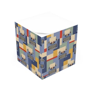 Può includere: Un cubo per appunti quadrato con un motivo ripetuto di macchine da scrivere blu vintage su uno sfondo di forme geometriche nei toni del rosso, giallo, azzurro e blu scuro. La superficie superiore è composta da fogli di carta bianca liscia.
