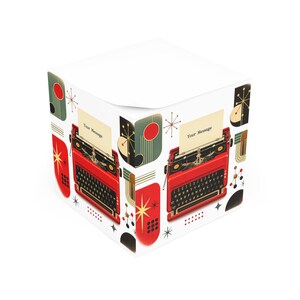 Può includere: Un cubo di foglietti adesivi quadrato con un motivo ripetuto di macchine da scrivere rosse vintage con tasti neri e un foglio di carta che mostra il testo Your Message, accentuato da cerchi rossi, forme geometriche nere e motivi a stella dorati.