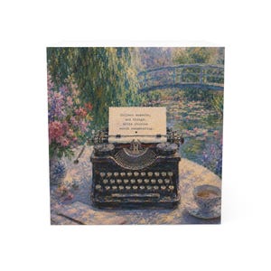 Può includere: Una macchina da scrivere nera in stile vintage su un tavolo con un foglio che riporta la scritta "Collect moments, not things. Write stories worth remembering.". Il set include un vaso di fiori e una tazza da tè su sfondo dipinto.