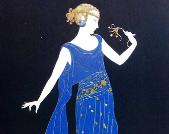 Puede incluir: Una mujer con un vestido azul con detalles dorados se encuentra de pie sobre un fondo negro. El vestido tiene un estampado floral y una larga cola. La mujer sostiene una pequeña flor en su mano.