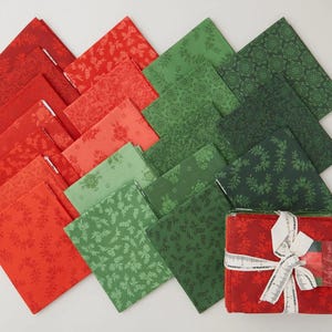 May include: A collection of red and green fabric squares with floral patterns. The fabrics are arranged in a gradient, transitioning from red to green. A bundle of red fabric is tied with a white ribbon and a tag.