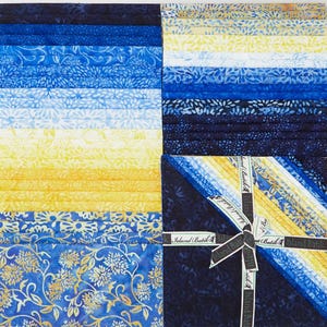 May include: A stack of square fabric cuts featuring a gradient of blue, yellow, and white batik patterns. The collection includes floral and abstract motifs, with a ribbon printed with the text Island Batik tied around the fabric bundle.