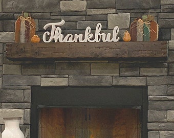 Puede incluir: Una repisa de madera rústica con un letrero de madera blanco que dice "Thankful". La repisa está decorada con pequeñas calabazas naranjas y un fuego arde en la chimenea de abajo.