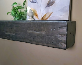 Puede incluir: Una estantería de madera gris oscuro con un acabado desgastado. La estantería está montada en una pared y tiene una pequeña figurita de pájaro blanco en la parte superior.