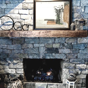 Puede incluir: Una repisa de madera r&uacute;stica sobre una chimenea de piedra con una pantalla de fuego de metal negro y un inserto de chimenea de gas. La repisa est&aacute; decorada con tres anillos de metal negro.