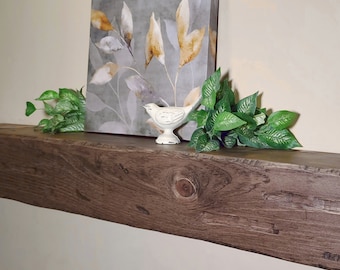 Puede incluir: Una repisa de madera rústica de color marrón con una figurita de pájaro blanco y una pintura acuarela enmarcada de hojas en tonos grises y amarillos.