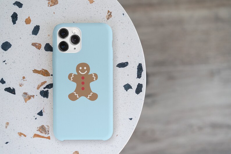 May include: A light blue phone case featuring a gingerbread man design. The gingerbread man is brown with red buttons and a white smile.