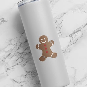 May include: White stainless steel tumbler with a gingerbread man design. The gingerbread man is brown with red buttons and a white smile.