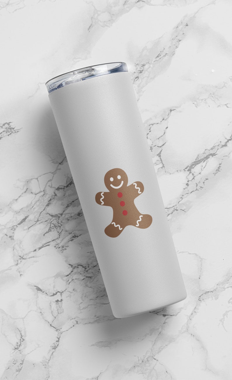 May include: White stainless steel tumbler with a gingerbread man design. The gingerbread man is brown with red buttons and a white smile.