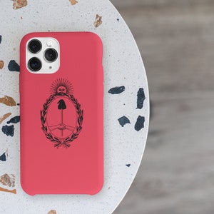 Puede incluir: Una funda roja para iPhone con un dise&ntilde;o negro del escudo de armas de Argentina. La funda tiene un recorte para el objetivo de la c&aacute;mara y un borde elevado alrededor de los bordes.