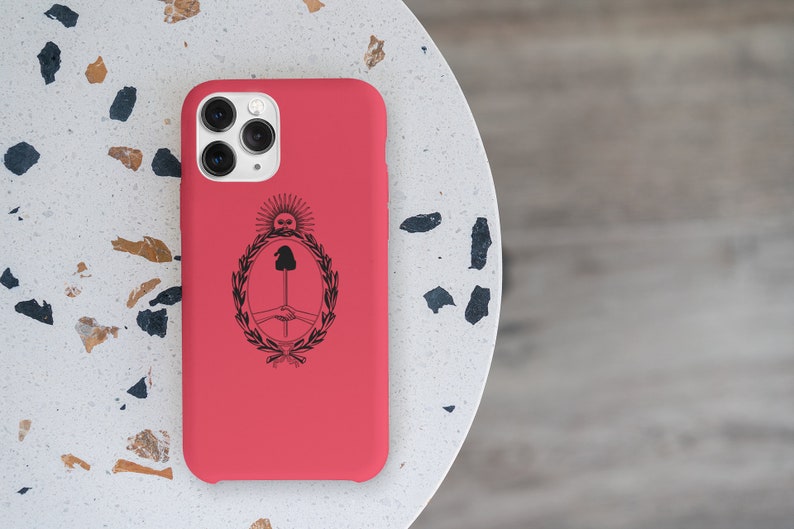 Puede incluir: Una funda roja para iPhone con un dise&ntilde;o negro del escudo de armas de Argentina. La funda tiene un recorte para el objetivo de la c&aacute;mara y un borde elevado alrededor de los bordes.