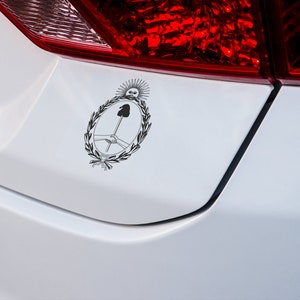 Puede incluir: Una pegatina en blanco y negro del escudo de armas de Argentina en un parachoques de coche blanco.