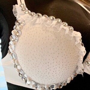 May include: White bra with a white ruffle trim and a beaded design around the cups. The beads are clear and white.