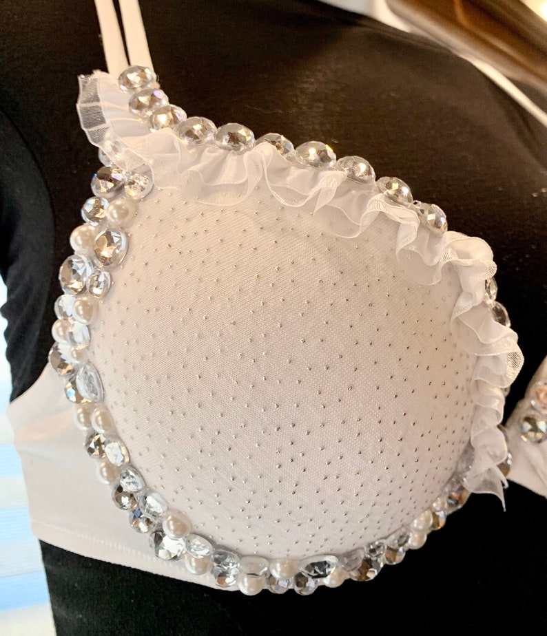 May include: White bra with a white ruffle trim and a beaded design around the cups. The beads are clear and white.