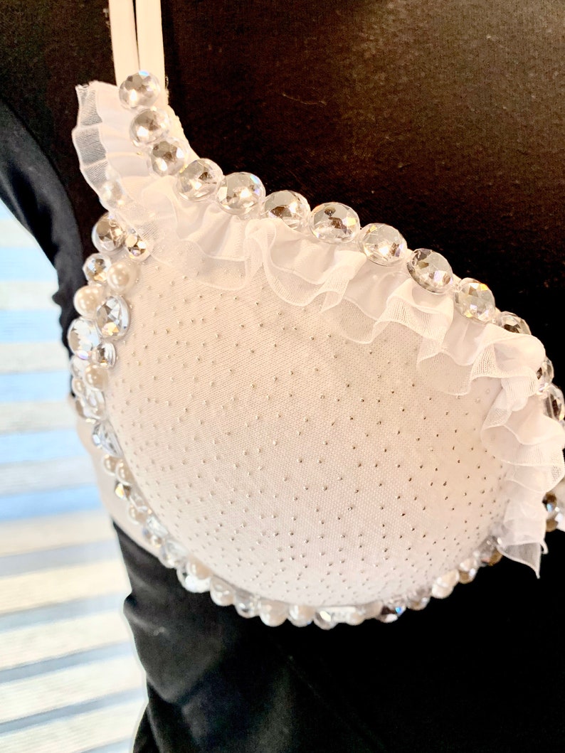 May include: White bra with a ruffled trim and clear rhinestones. The bra is made of a sheer fabric with a dotted pattern.