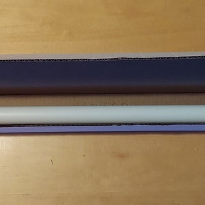 May include: A white cardboard box with the top open, revealing a long, white, cylindrical object with red and white end caps. The object is lying horizontally in the box.