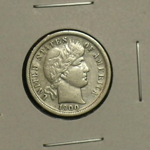 May include: A silver United States dime from 1900, featuring a profile of a woman with a laurel wreath. The coin is in a protective holder, with the words "UNITED STATES OF AMERICA" and the year "1900" visible.