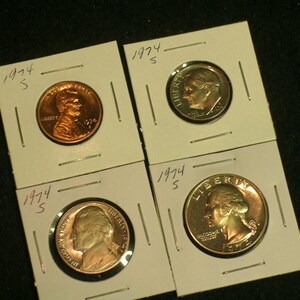 May include: Four coins from 1974, including a penny, dime, nickel, and quarter, each in a protective holder. The coins are displayed against a dark background. The year and the letter "S" are written on each holder.