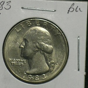 May include: A 1983 United States quarter coin, featuring a profile of George Washington, the words "LIBERTY" and "IN GOD WE TRUST". The coin is in a protective holder with handwritten notes.