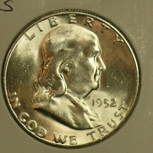 May include: A silver half dollar coin featuring a profile of Benjamin Franklin with the inscription "LIBERTY" above and "IN GOD WE TRUST" below. The year "1952" is inscribed on the right side of the coin.