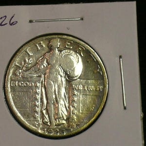 May include: A silver 1926 Walking Liberty Half Dollar coin. The coin features a profile of Liberty walking forward, holding a branch in her right hand and a shield in her left hand. The inscription "IN GOD WE TRUST" is visible on the coin.