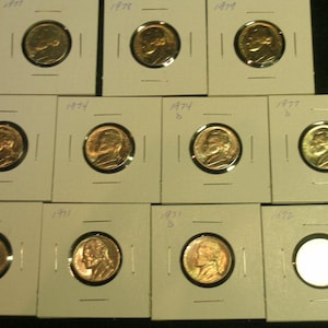 May include: A collection of circulated Jefferson nickels in protective cardboard holders. The coins are dated from the late 1960s to the 1970s. The image shows the obverse of the coins, featuring the profile of Thomas Jefferson.