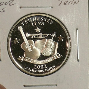 May include: A silver Tennessee quarter coin featuring musical instruments: a guitar, trumpet, and violin. The coin is inscribed with "Tennessee 1796" and "Musical Heritage 2002". The coin is in a protective holder.