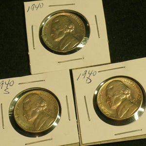 May include: Three 1940 Jefferson nickel coins in protective holders. The coins are gold-colored with a profile of Thomas Jefferson on the front. Each holder is labeled with the year and a mint mark.