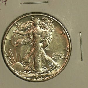 May include: A silver 1939 Walking Liberty half dollar coin. The coin features a detailed depiction of Lady Liberty walking towards the sun, with the words "IN GOD WE TRUST". The coin is in a protective holder.