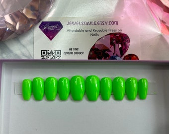 Op de afbeelding: Tien felgroene press-on nagels in een kistvorm, gepresenteerd in een witte doos. De nagels zijn in een rij gerangschikt, met de punten naar de kijker gericht. De doos heeft een witte achtergrond en een paarse rand.