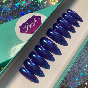 May include: A set of ten blue iridescent stiletto false nails in a teal box with the text "Jewels Nails" on the lid.