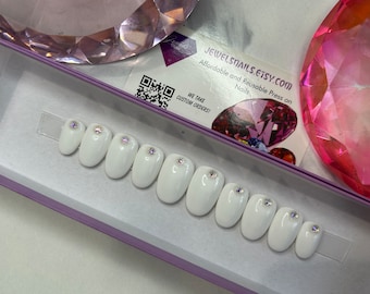 Könnte beinhalten: Ein Set mit zehn weißen, ovalen Press-on-Nägeln mit klaren, schillernden Strasssteinen auf jedem Nagel. Die Nägel werden in einer violetten Box mit einer Visitenkarte präsentiert, auf der steht: "JewelSnails.Etsy.com Erschwingliche und wiederverwendbare Press-on-Nägel Wir nehmen individuelle Bestellungen entgegen!"