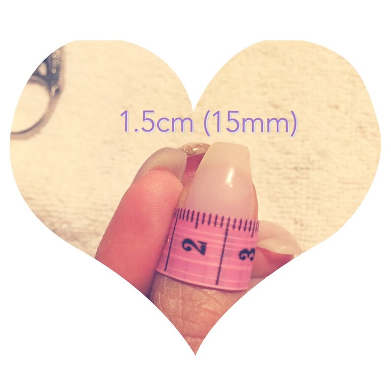 May include: A close-up of a finger with a pink measuring tape wrapped around it. The tape reads "2" and "3". The text "1.5cm (15mm)" is written above the finger.