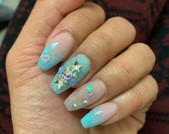 May include: Close-up of a hand with long, light blue ombre nails decorated with glitter and silver stars. The nails are shaped into a coffin shape.