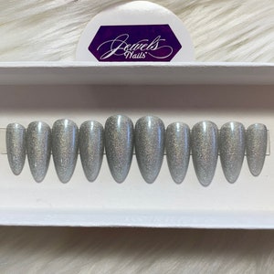 May include: Set of ten silver glitter stiletto false nails in a white box. The box has the text "Jewels Nails" on it.